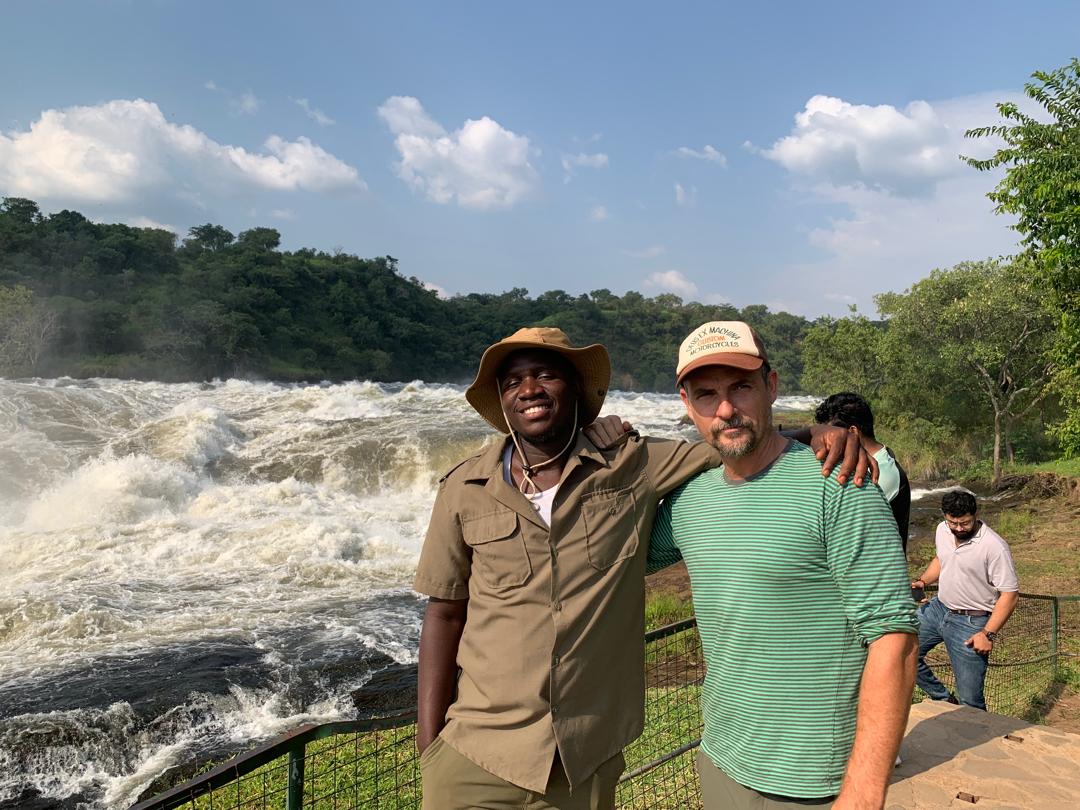 Deogratious and a guest beside a rushing waterfall