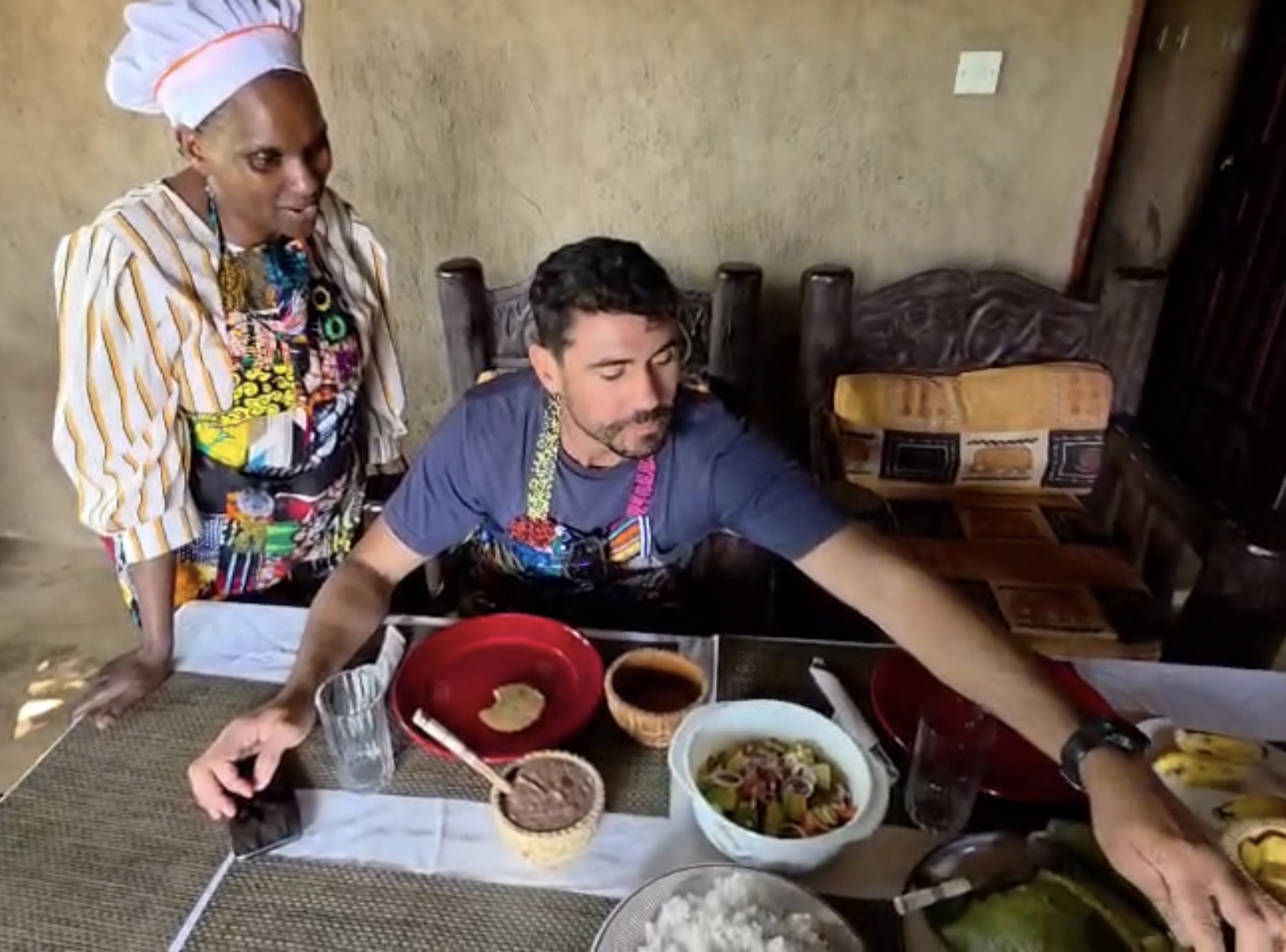 Aine at the table with a guest, sharing the Ugandan dishes they prepared together