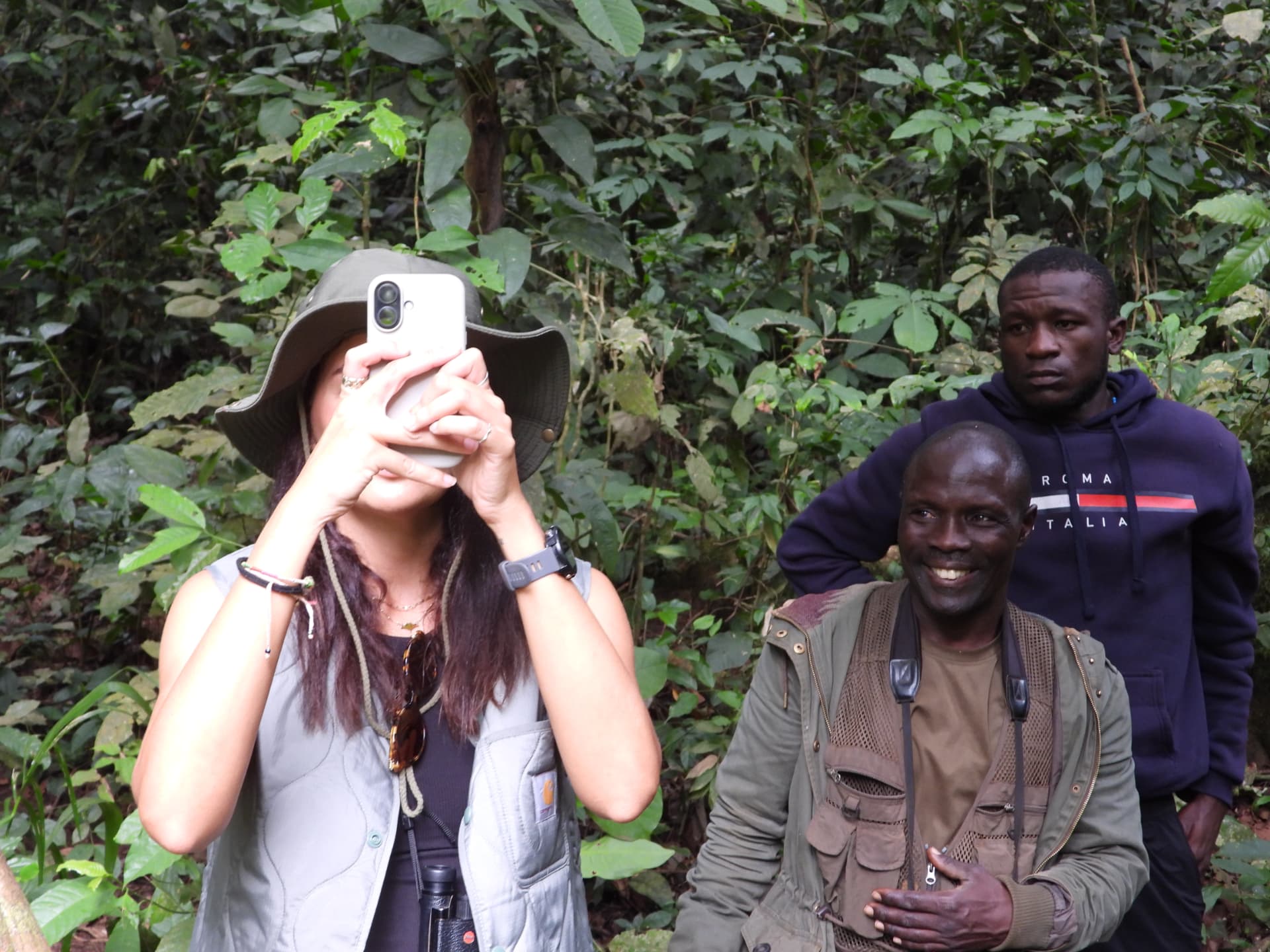 Traveller photographing chimpanzees while two local guides look on in the forest