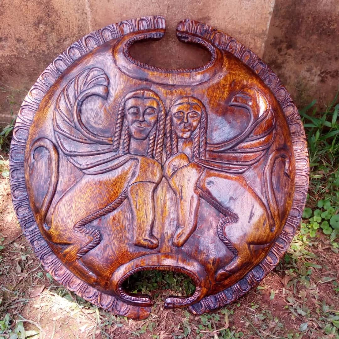 Polished carved wooden shield by Silver with two winged figures in relief