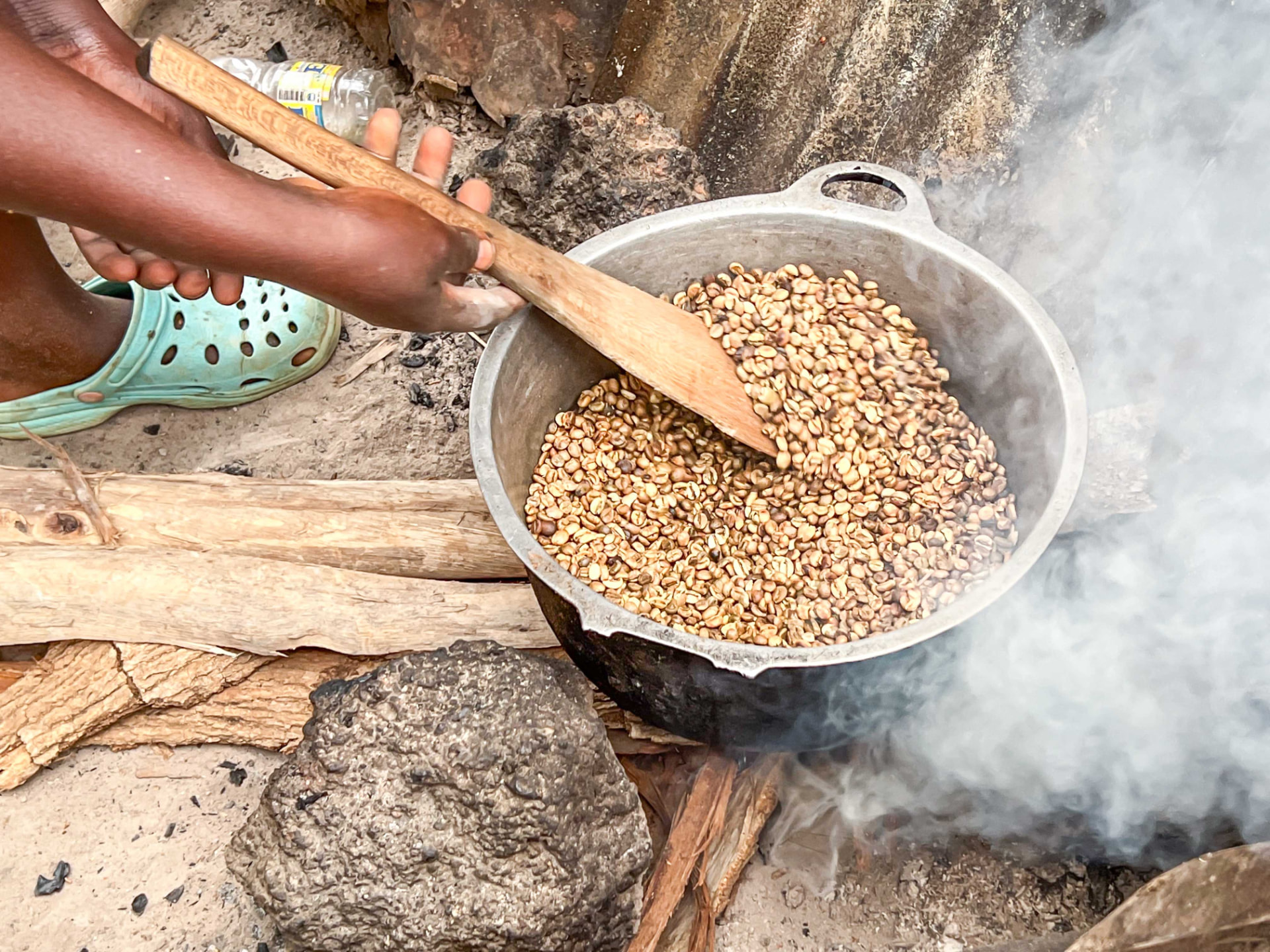 Coffee beans being roasted over a wood fire, stirred with a wooden paddle